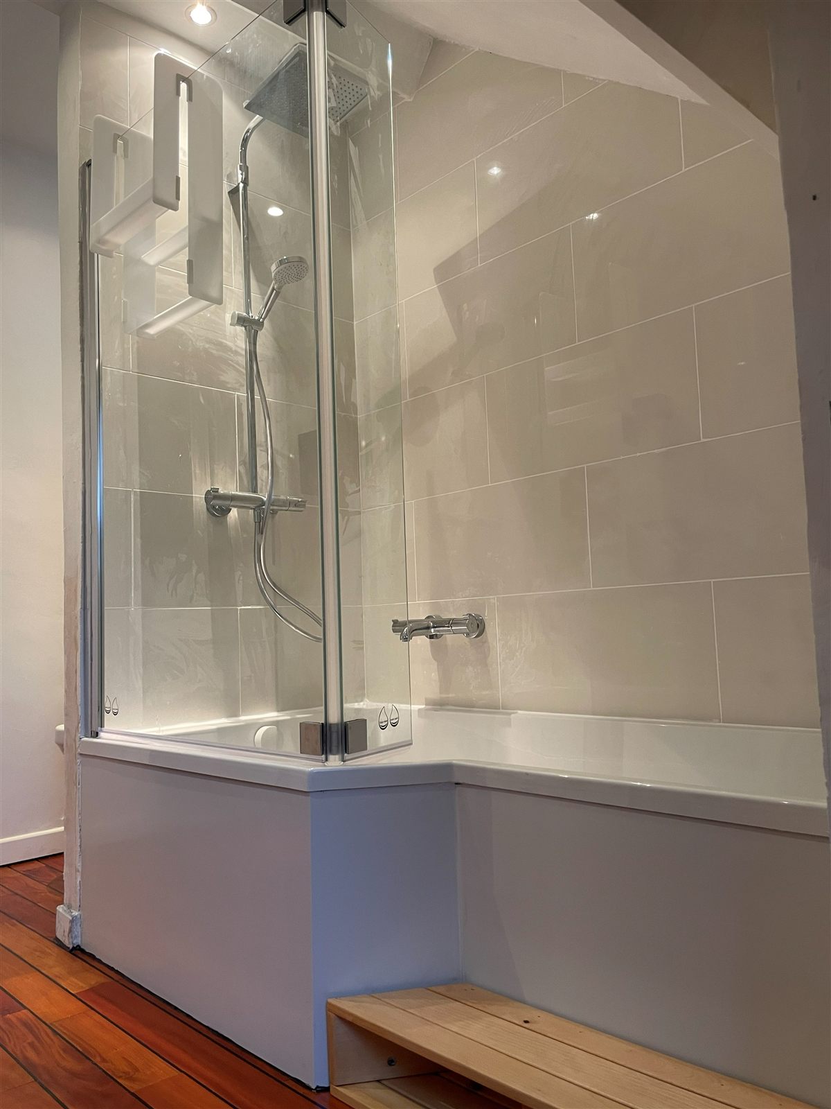 Baignoire avec pare-douche en verre, colonne thermostatique et faïence claire dans un appartement ancien