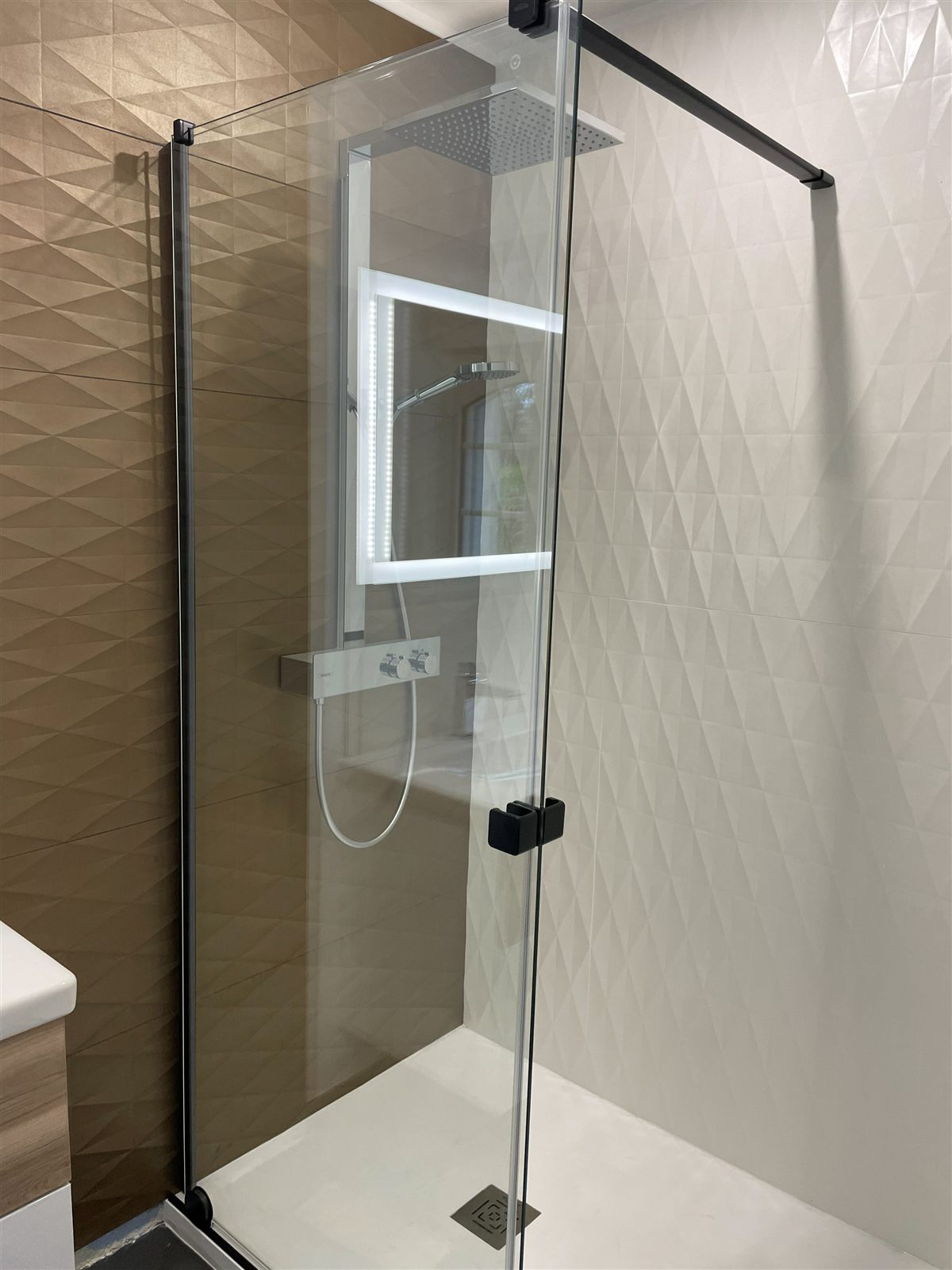 Douche fermée par une paroi vitrée à profilés noirs, faïence à relief géométrique et colonne thermostatique