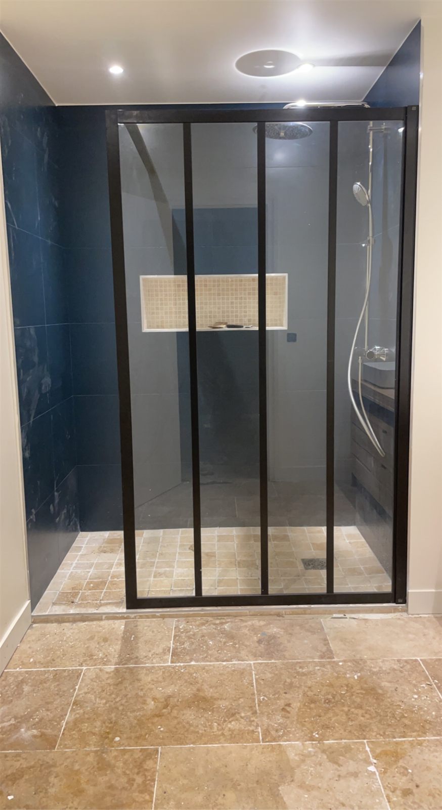 Douche à l'italienne avec paroi vitrée type verrière noire, faïence bleu nuit et sol travertin