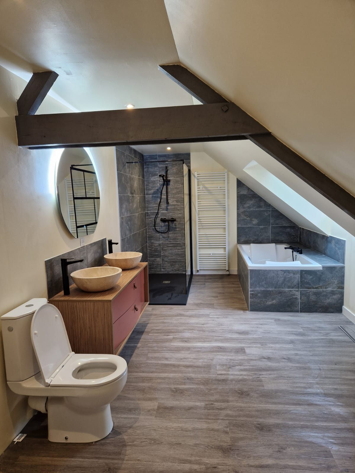 Salle de bain sous combles avec poutres apparentes, baignoire d'angle et douche carrelée ardoise